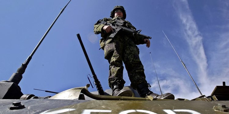 TOPSHOT - A KFOR soldier stands on an armoured vehicle as UN troops block all access to the ethnic Albanian village of Cabra, 10km west of the flashpoint city of Kosovska Mitrovica 21 March 2004, where the funeral of two children who have drowned last Tuesday are taking place. Thousands of Kosovars gathered here in silent grief on Sunday to bury two ethnic Albanian children, whose alleged death at the hands of Serb attackers sparked deadly ethnic violence last week. NATO helicopters hovered over the northern village of Cabra, while checkpoints were set up at the entrance to the picturesque village amid fears that the funerals could spark another wave of violence.  AFP PHOTO/KOCA SULEJMANOVIC (Photo by KOCA SULEJMANOVIC / AFP) (Photo by KOCA SULEJMANOVIC/AFP via Getty Images)